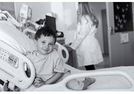 Young boy smiling in hospital bed with physician in background