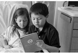 Young girl in hospital bed with older brother reading to her 
