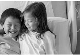 Young girl and brother in hospital bed laughing 