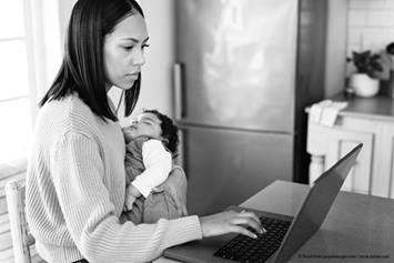 mother holding her baby in one hand while working on the computer