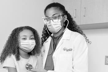 A patient and doctor at a well visit appointment. Both are wearing masks and the doctor is wearing protective eyewear.